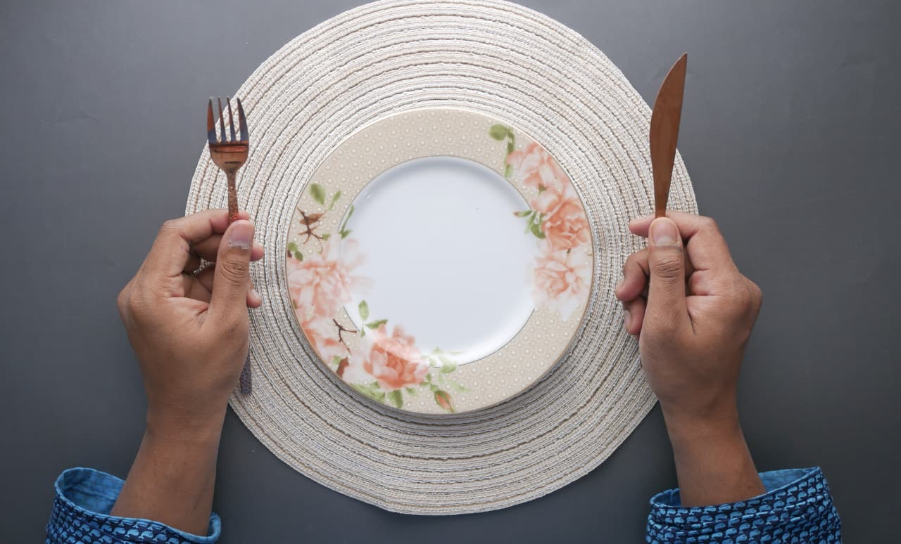 Piatto vuoto a tavola con mani e posate, simbolo del rapporto con il binge eating